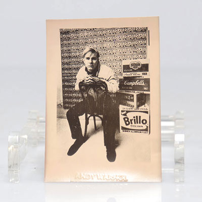 Andy Warhol. (d'après - after).  Photographie en noir et blanc représentant Andy Warhol assis à côté de cartons de Brillo et de Campbell’s.